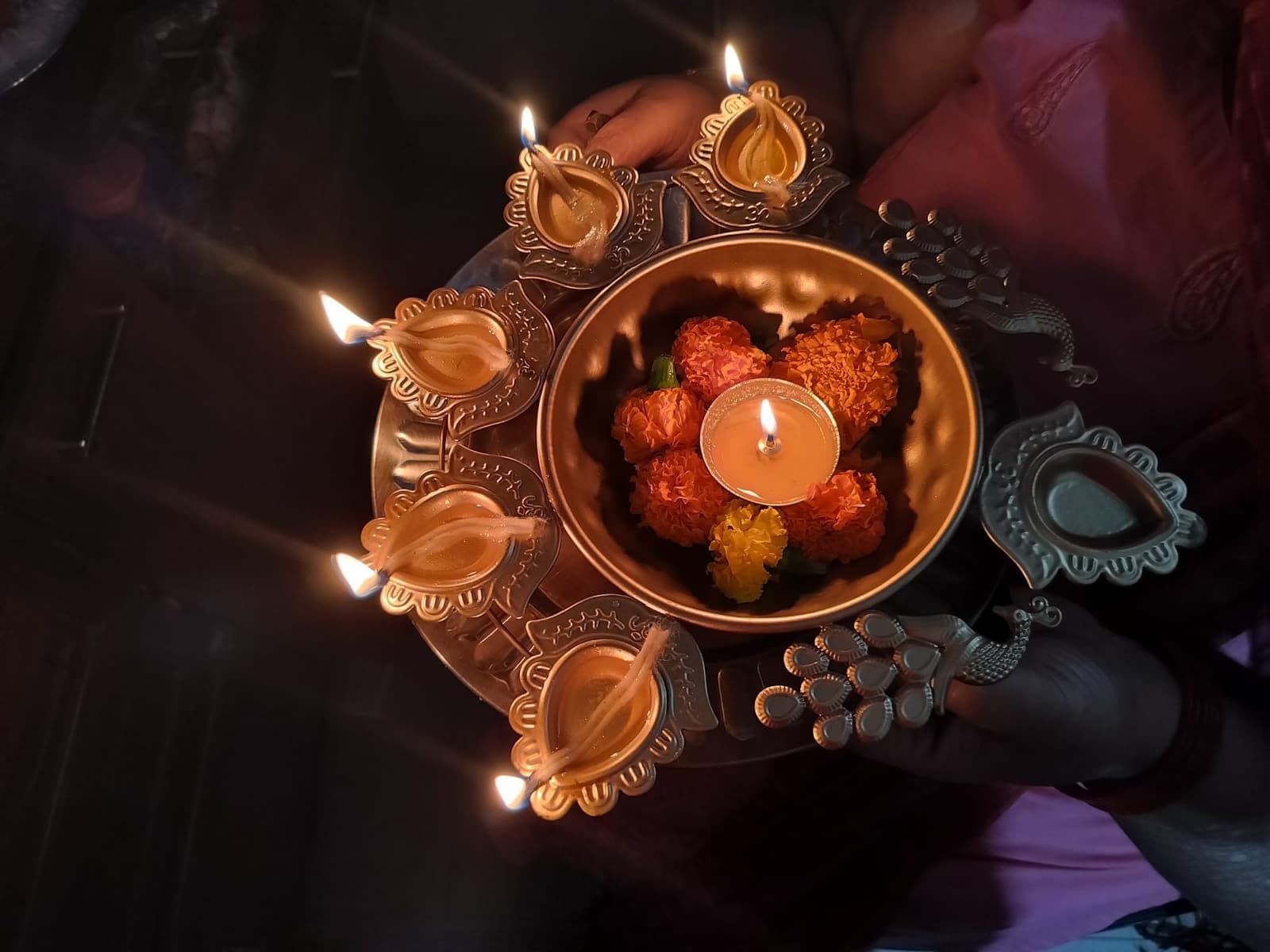 A brass puja thali with lit diyas and flowers